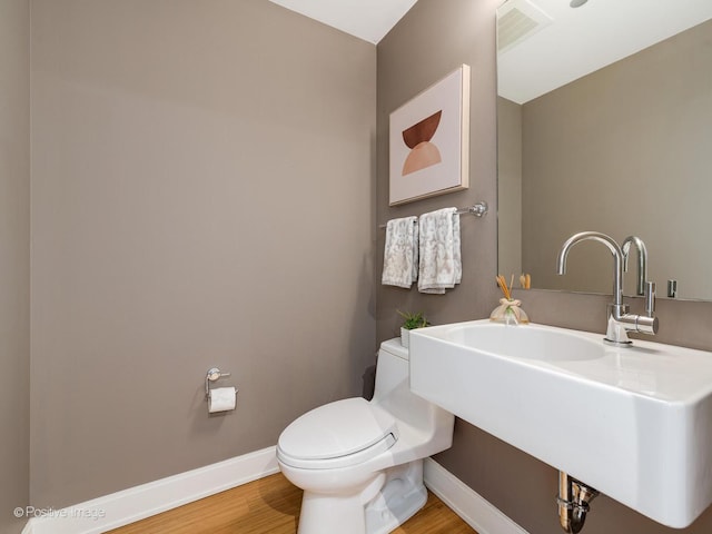 half bathroom with toilet, a sink, visible vents, wood finished floors, and baseboards