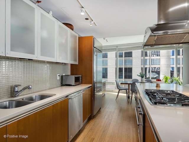 kitchen featuring a sink, light countertops, appliances with stainless steel finishes, backsplash, and brown cabinetry