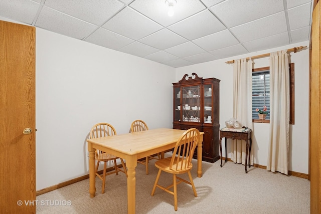 dining room with a drop ceiling, light carpet, and baseboards