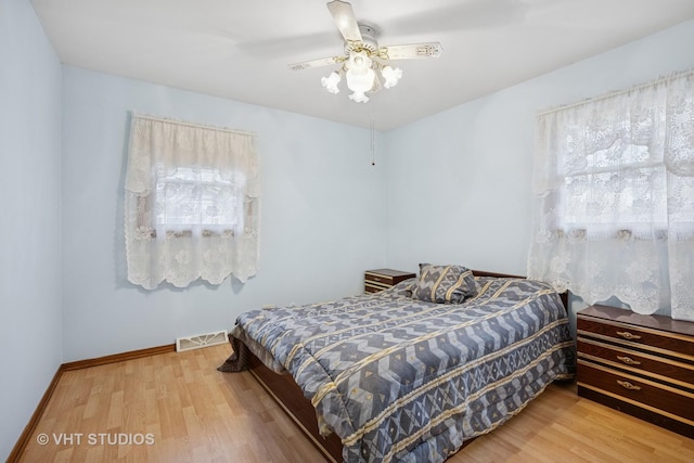 bedroom featuring a ceiling fan, visible vents, baseboards, and wood finished floors