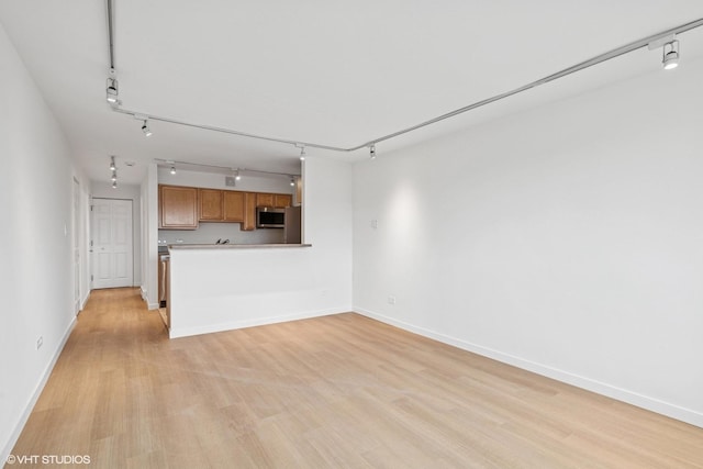 unfurnished living room featuring light wood-style floors, baseboards, and rail lighting