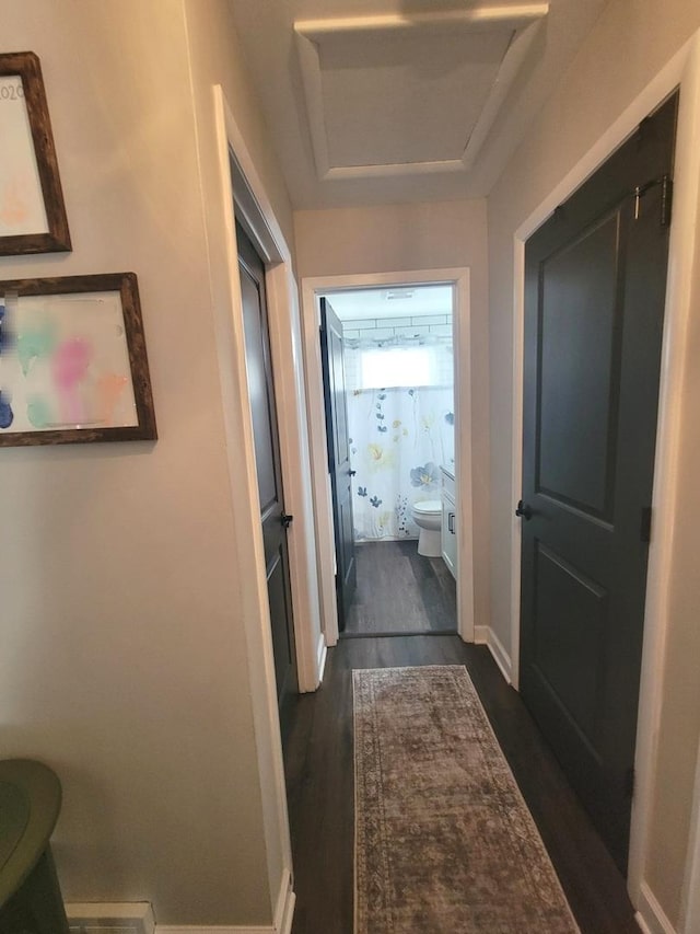 corridor with baseboards, attic access, and dark wood-style flooring