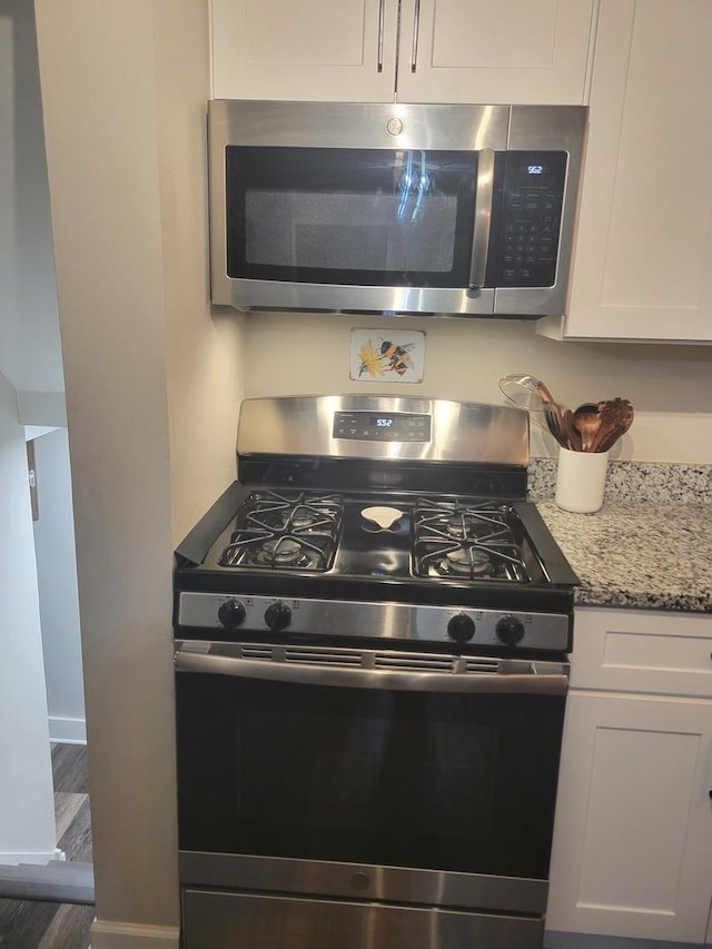 kitchen with light stone counters, wood finished floors, baseboards, white cabinets, and appliances with stainless steel finishes