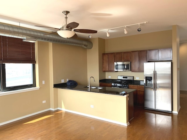 kitchen with dark countertops, dark wood-style floors, appliances with stainless steel finishes, a peninsula, and a sink