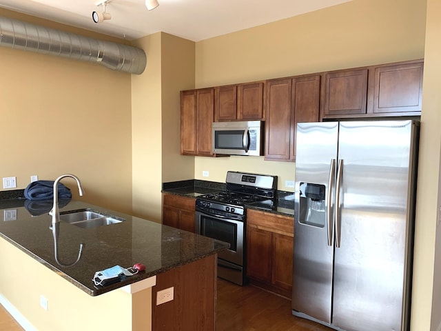 kitchen featuring dark wood-style floors, appliances with stainless steel finishes, dark stone countertops, a peninsula, and a sink