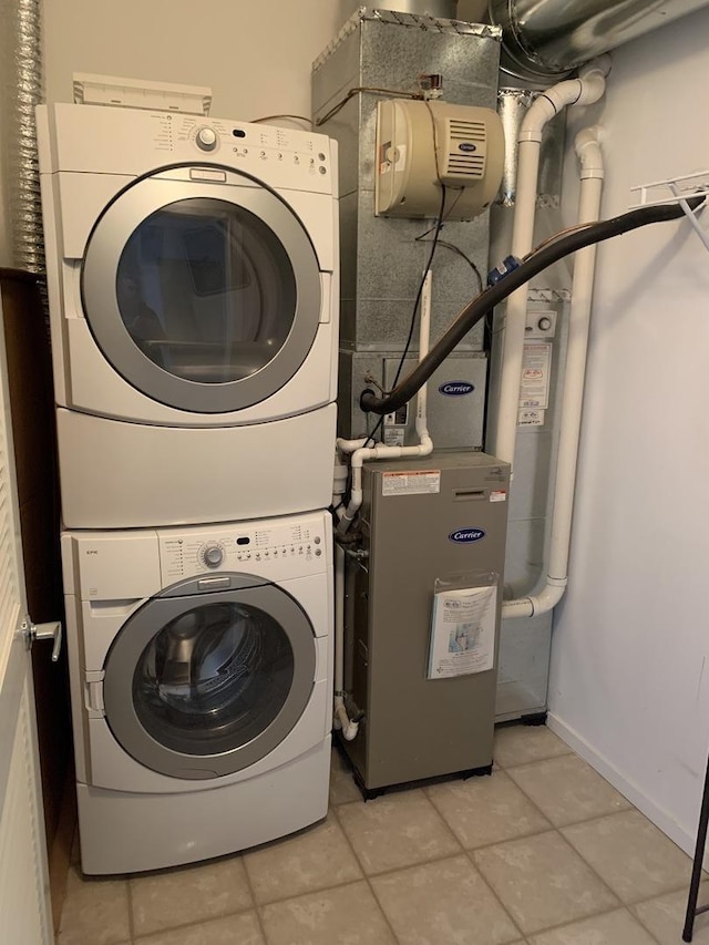 laundry area featuring light tile patterned floors, laundry area, stacked washing maching and dryer, and baseboards