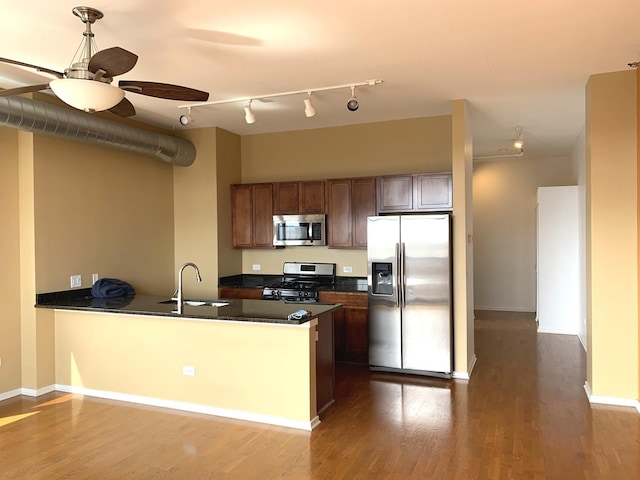 kitchen with dark wood-style flooring, dark countertops, appliances with stainless steel finishes, a sink, and a peninsula