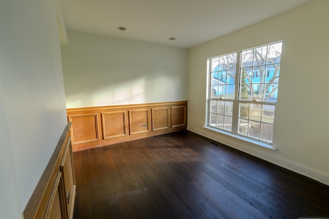 empty room featuring dark wood-style floors, baseboards, and visible vents