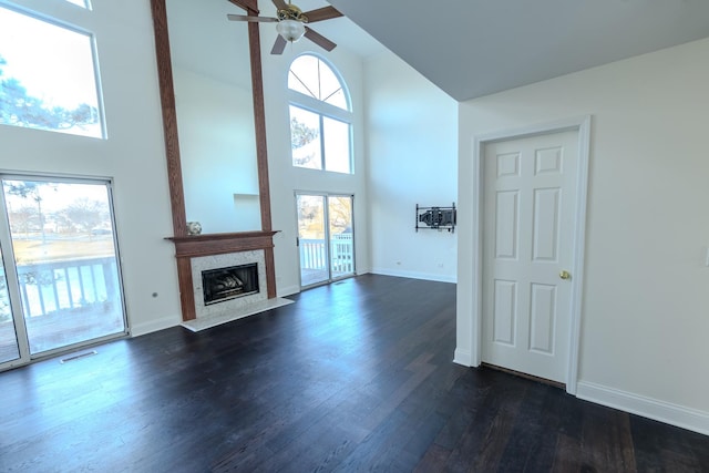 unfurnished living room with dark wood-style flooring, visible vents, a premium fireplace, high vaulted ceiling, and baseboards