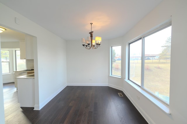 unfurnished dining area featuring dark wood-type flooring, visible vents, baseboards, and an inviting chandelier