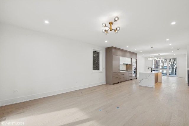 unfurnished living room with an inviting chandelier, light wood-style flooring, baseboards, and recessed lighting