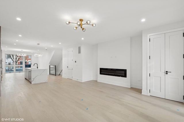 unfurnished living room with visible vents, a glass covered fireplace, an inviting chandelier, light wood-type flooring, and recessed lighting