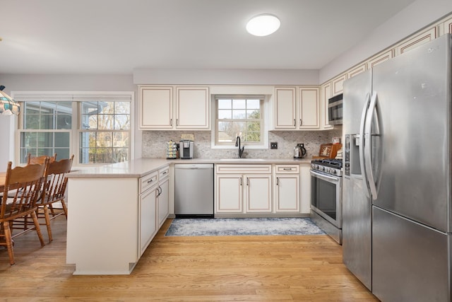 kitchen with a peninsula, a sink, light wood-style floors, light countertops, and appliances with stainless steel finishes