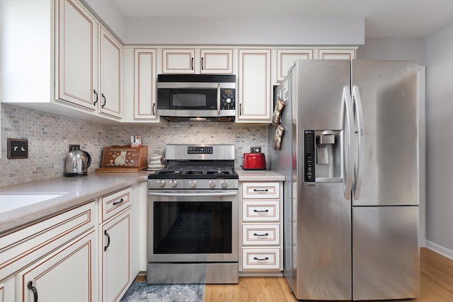 kitchen featuring stainless steel appliances, tasteful backsplash, light countertops, and light wood-style flooring