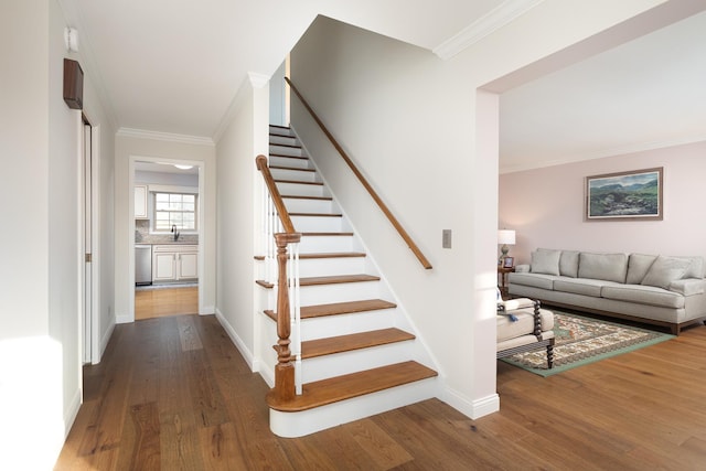 stairs with baseboards, wood finished floors, and crown molding