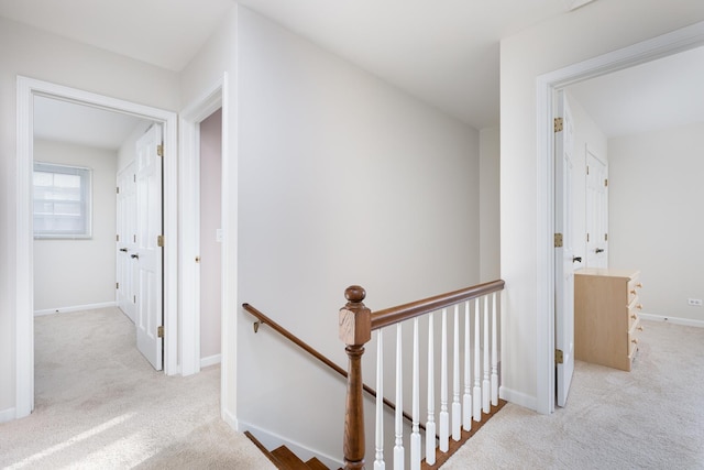 hall with carpet floors, baseboards, and an upstairs landing