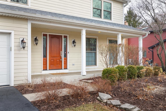 view of exterior entry with covered porch, a shingled roof, and a garage