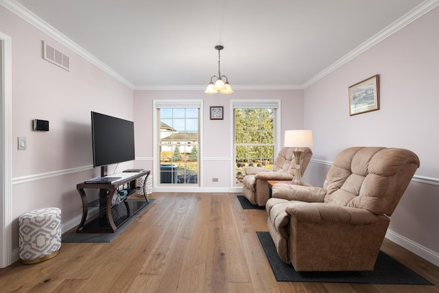 living area with baseboards, visible vents, wood finished floors, crown molding, and a chandelier