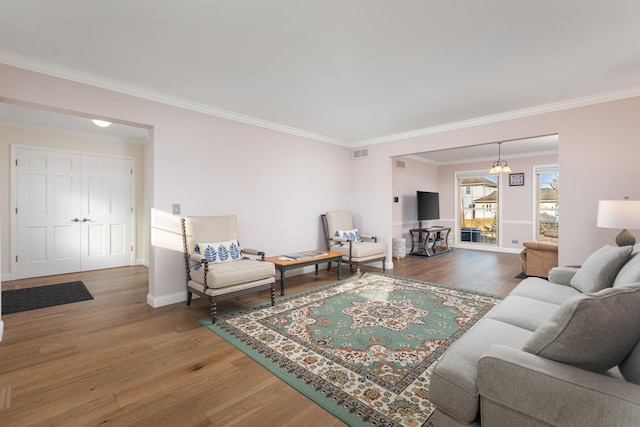 living room with baseboards, wood finished floors, visible vents, and crown molding