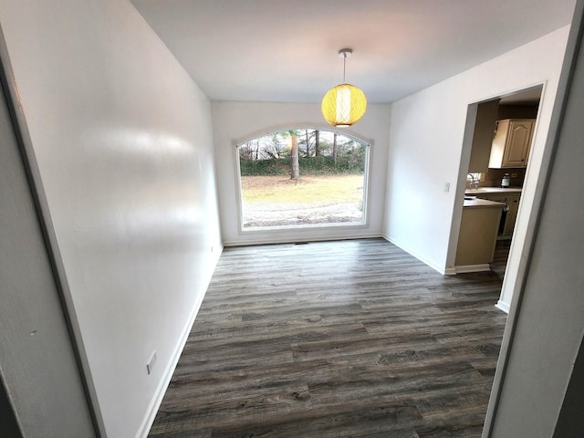 unfurnished dining area with baseboards and dark wood finished floors