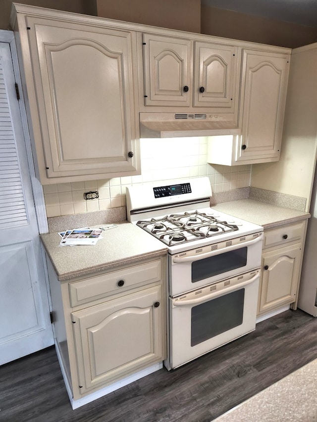 kitchen featuring under cabinet range hood, double oven range, decorative backsplash, and light countertops