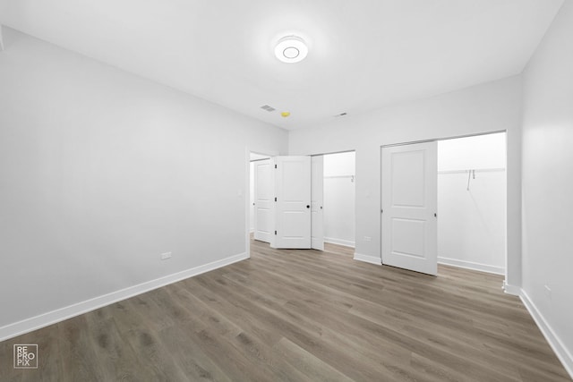 unfurnished bedroom with wood finished floors, baseboards, and two closets