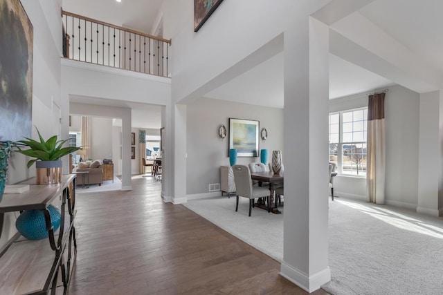 entryway featuring carpet flooring, a towering ceiling, baseboards, and wood finished floors