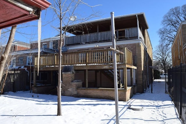 snow covered rear of property with stairway, a wooden deck, fence, and brick siding