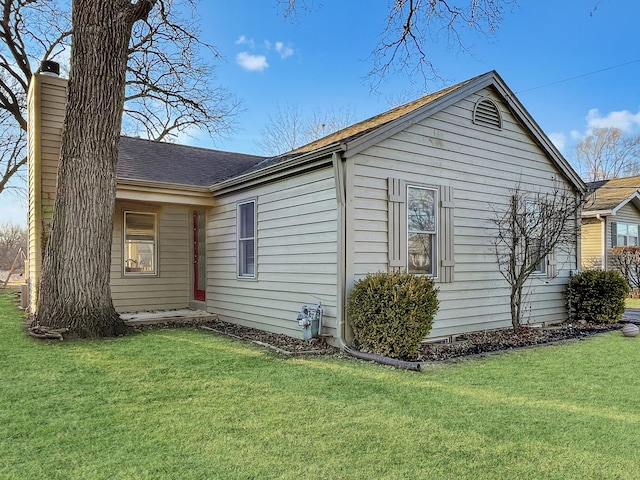 view of side of property with roof with shingles, a chimney, and a yard