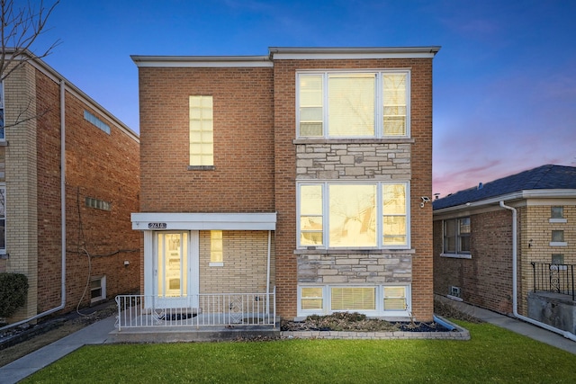 front of property at dusk featuring stone siding, a lawn, and brick siding