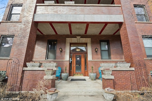 view of exterior entry with a porch and brick siding