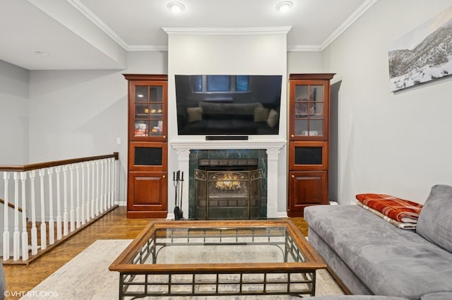 living area featuring a warm lit fireplace, ornamental molding, and wood finished floors