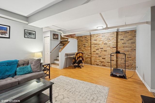 living room featuring stairs, brick wall, light wood-style flooring, and baseboards