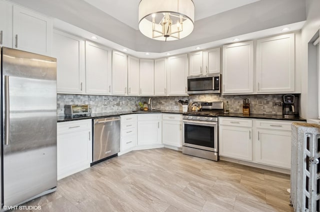 kitchen with a notable chandelier, stainless steel appliances, a sink, tasteful backsplash, and dark countertops