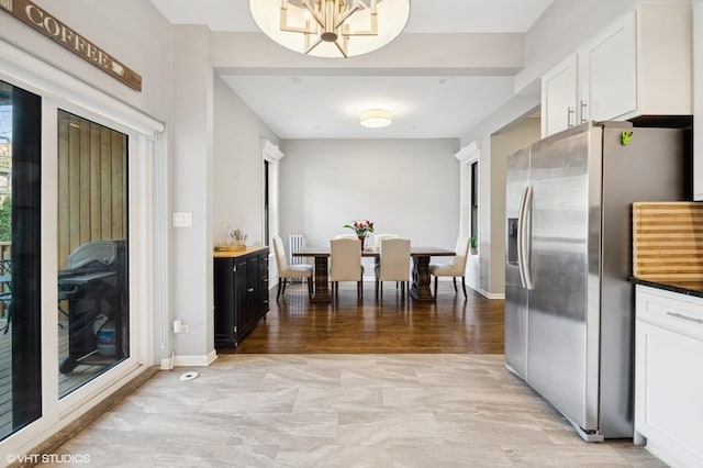 kitchen featuring dark countertops, white cabinetry, a chandelier, stainless steel fridge, and baseboards