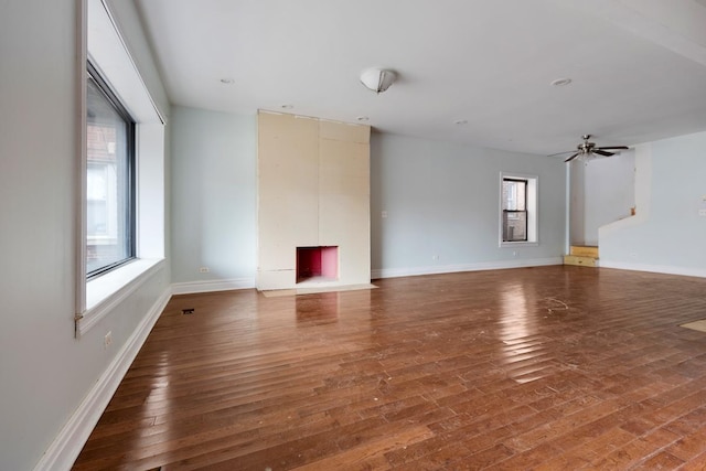 unfurnished living room with a ceiling fan, wood-type flooring, a fireplace, and baseboards