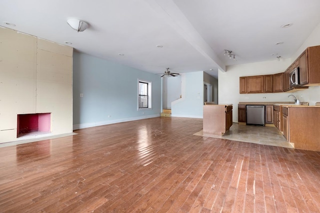 unfurnished living room with baseboards, a sink, light wood finished floors, and ceiling fan