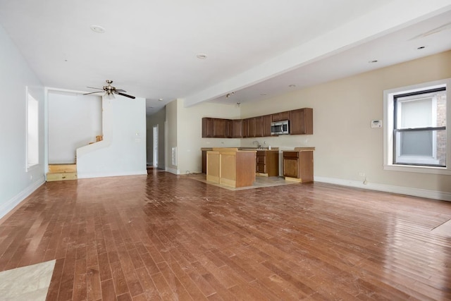 unfurnished living room featuring a sink, light wood-style flooring, baseboards, and a ceiling fan