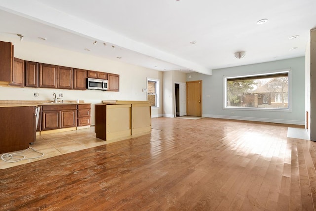 kitchen featuring open floor plan, stainless steel microwave, light wood-style flooring, and baseboards