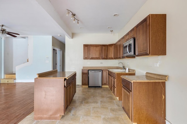 kitchen with a center island, stainless steel appliances, brown cabinetry, a ceiling fan, and a sink