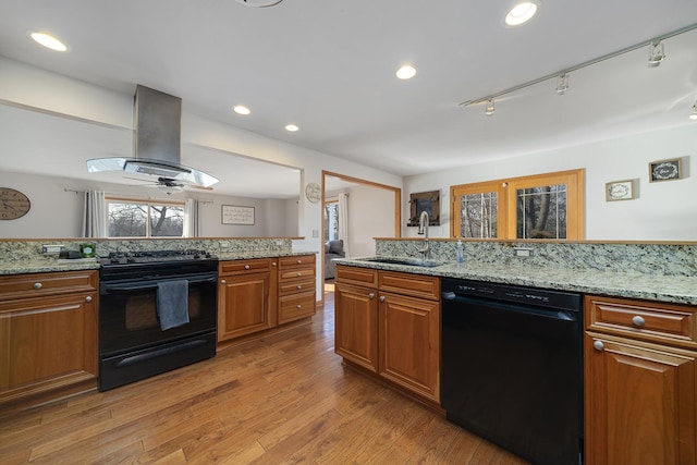 kitchen with brown cabinets, island exhaust hood, a sink, light wood-type flooring, and black appliances