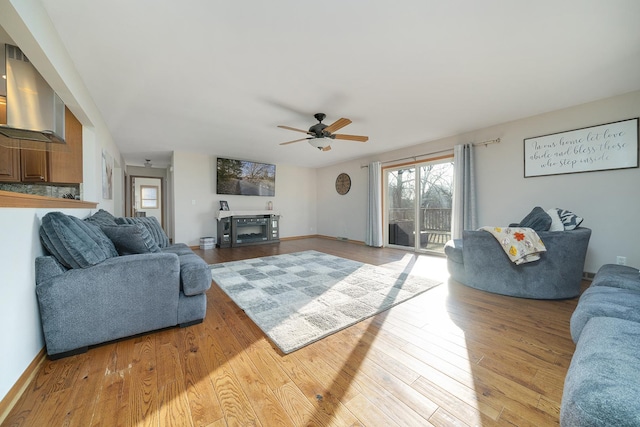 living area with light wood-style flooring, baseboards, and a ceiling fan