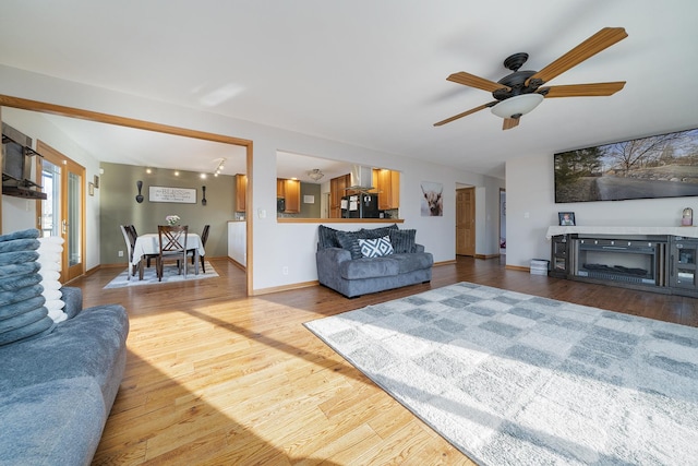 living room featuring ceiling fan, baseboards, and wood finished floors