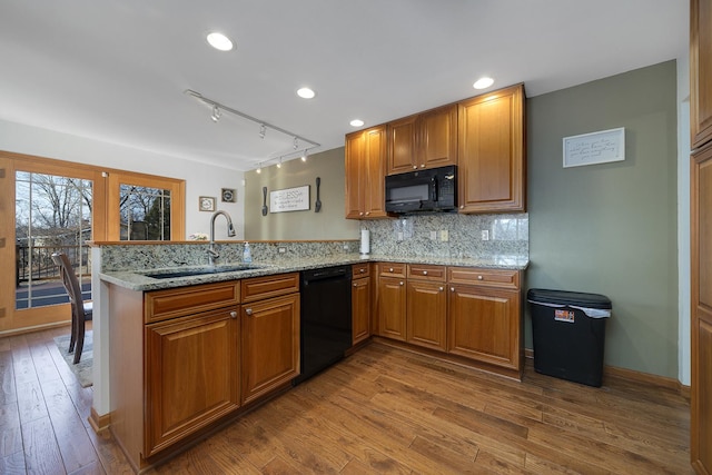 kitchen with brown cabinets, wood finished floors, a peninsula, black appliances, and a sink