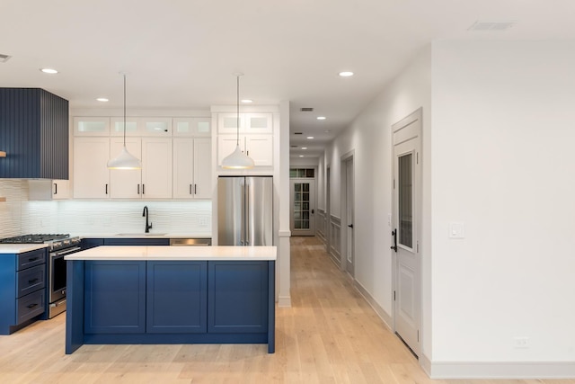 kitchen with appliances with stainless steel finishes, blue cabinets, light countertops, white cabinetry, and a sink