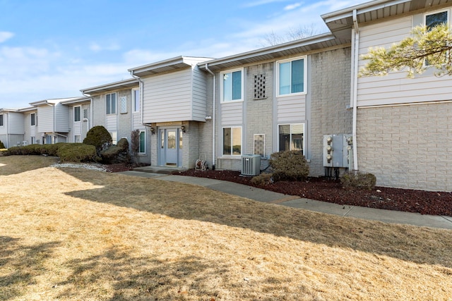 view of property featuring brick siding, a front lawn, and central air condition unit