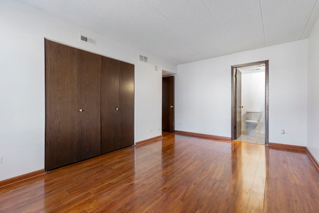 unfurnished bedroom featuring a closet, visible vents, a textured ceiling, wood finished floors, and baseboards