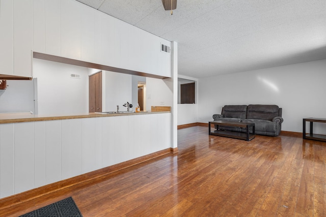 living area with wood-type flooring, visible vents, ceiling fan, and baseboards