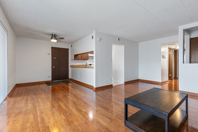 unfurnished living room with a textured ceiling, light wood finished floors, and baseboards