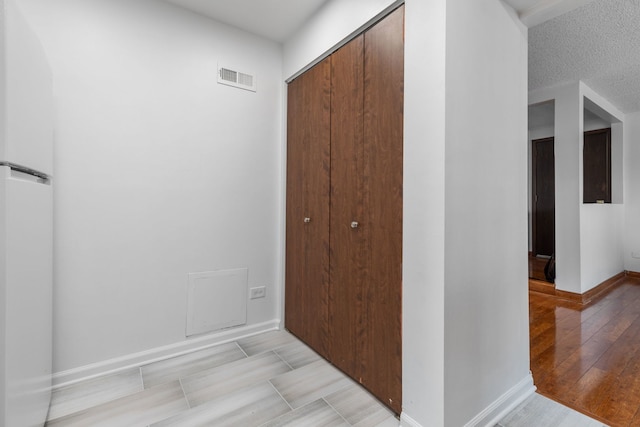 corridor featuring light wood-type flooring, baseboards, visible vents, and a textured ceiling